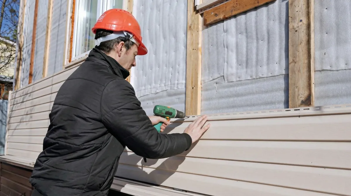 Siding replacement professional using a power drill to install new tan vinyl siding on a home exterior in Cincinnati, OH